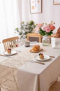 Close-up of linen tablecloth with tassel fringe and delicate crochet lace table runner