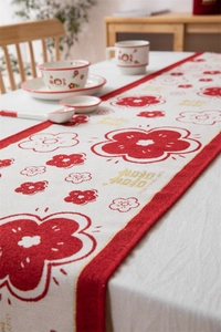 Detail van witte tafelloper met rode bloemmotieven en een feestelijke goudkleurige rand