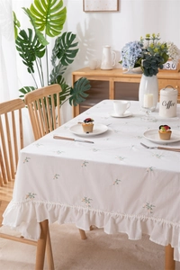 Detail of white cotton tablecloth with floral embroidery and ruffle edges in rustic style