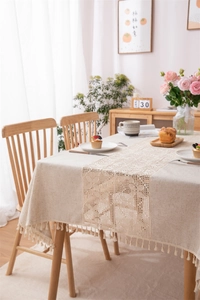 Detail of linen tablecloth with beige floral lace patchwork and elegant fringe tassels