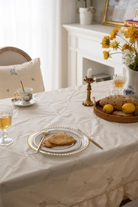Close-up of beige cotton tablecloth with floral embroidery and ruffled edge detail