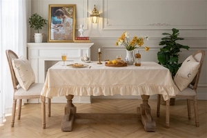 Detailed view of cream cotton tablecloth with elegant ruffled edges and floral texture