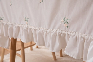Detail of white cotton tablecloth featuring floral embroidery and ruffled edge design