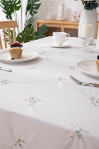Detail of white cotton tablecloth featuring elegant floral embroidery and ruffled edges
