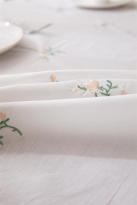 Detail of floral embroidery on white cotton tablecloth with delicate ruffled edges