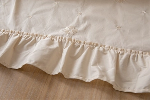 Macro view of light apricot cotton tablecloth featuring ruffled edges and floral embroidery