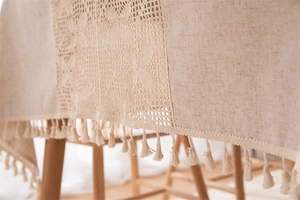 Close-up of beige linen tablecloth featuring intricate lace splicing and tassel edge detail