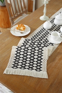 Detail of bohemian table runner with woven black and white diamond patterns and tassels