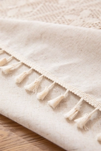 Detailed close-up of beige linen tablecloth featuring woven patterns and tassel fringe edge