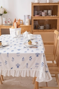 Detail showing white cotton tablecloth with blue floral prints and elegant ruffle edges