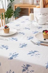 Detail of white cotton tablecloth featuring blue floral embroidery and ruffle edges