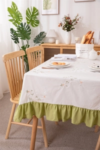 Detail of floral embroidery and green ruffled edge on apricot cotton tablecloth