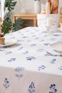 Detailed close-up of blue floral embroidery on white cotton tablecloth with ruffles
