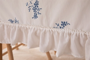 Detail of blue floral embroidery and ruffled edge on a white cotton tablecloth