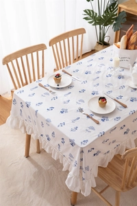 Detail of white cotton tablecloth with blue floral embroidery and ruffle edges