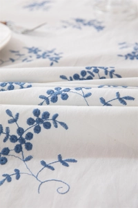 Close-up of blue floral embroidery on white cotton tablecloth with ruffled edges