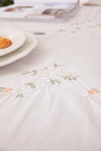 Detailed embroidery of floral patterns on an apricot cotton tablecloth with ruffled edges