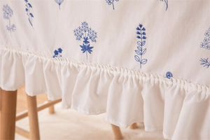 Detailed close-up of white cotton tablecloth with blue floral embroidery and ruffle edges