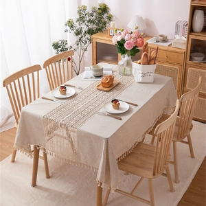 Linen table runner with crochet lace and tassels on a cream rectangular tablecloth