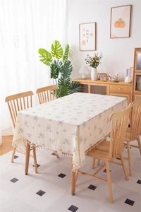 Detail of beige floral cotton tablecloth with delicate fringe edges and dark leaf pattern