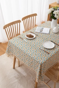Detailed view of rectangle tablecloth with orange floral print and elegant fringe edges