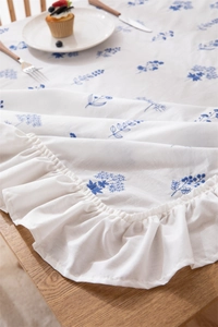 Close-up of white cotton tablecloth with blue floral embroidery and ruffled edge