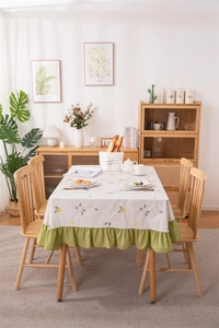Detail of floral embroidery and green ruffled hem on beige cotton linen tablecloth