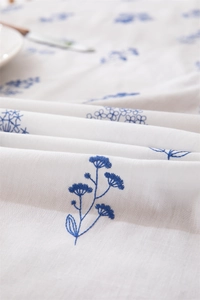 Close-up of blue floral embroidery on white cotton tablecloth with ruffle edge