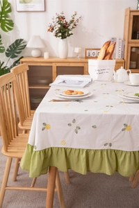 Close-up of floral embroidery and green ruffled edge on cotton dining tablecloth