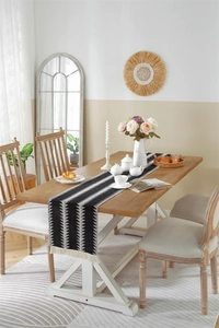 Detail of woven geometric pattern table runner with white tassels on a wooden surface