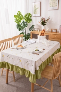 Close-up of cream cotton tablecloth with yellow floral embroidery and green ruffled edges
