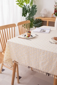 Close-up of small yellow daisy prints and cotton tassel fringe on rectangular tablecloth