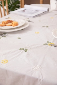 Detailed embroidery of yellow daisies and green leaves on cotton fabric tablecloth