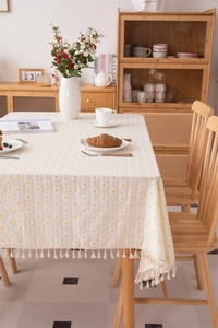 Close-up of cream floral cotton tablecloth featuring daisy print and handmade tassel edges