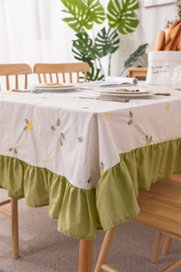 Detail of embroidered floral tablecloth featuring avocado green ruffled edges and cotton fabric