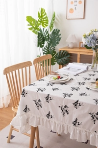 Close-up of white cotton tablecloth with black floral embroidery and ruffled edges