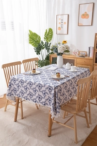 Detail of blue floral cotton linen tablecloth with elegant white fringe tassels on wood table