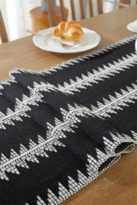Detail of woven table runner with black and white geometric embroidery on wood table