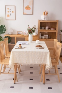 Macro view of beige floral jacquard tablecloth with tassel fringe in rustic dining room