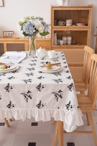 Close-up of white cotton tablecloth featuring black floral embroidery and ruffled edge trim