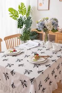 Detail of white cotton tablecloth featuring black floral embroidery and ruffled edges