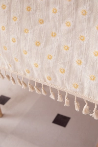 Close-up of cotton floral embroidery and tassel fringe on cream jacquard tablecloth