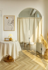 Detail of linen curtains and tablecloth with decorative tassels in a minimal home