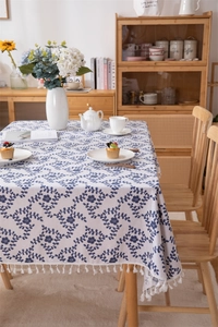 Detailed view of floral pattern tablecloth with cotton tassels on a wooden dining table