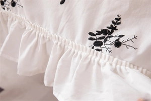 Detail of white cotton tablecloth showing black floral embroidery and ruffled edges