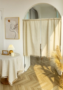 Detail of beige linen door curtain with tassels and matching tablecloth in soft sunlight