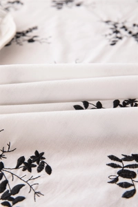 Detailed close-up of white cotton fabric with black floral embroidery and textured ruffles