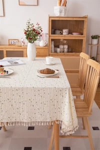 Macro detail of cream cotton tablecloth featuring yellow daisy patterns and beige fringe