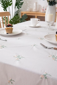 Close-up of floral embroidery on light beige cotton tablecloth with elegant ruffled edge
