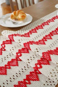 Detail of woven table runner with red heart embroidery and fringe on dark wood